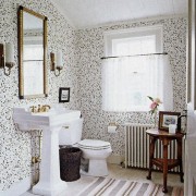 A well blended black and white bath with dainty wallpaper and a black and white striped rug to tie the space together.