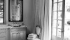 A well dressed bath with beautiful linen curtains and strategically placed chair to keep towels and other amenities handy. The large scale random size flooring adds to the texture in this bath.